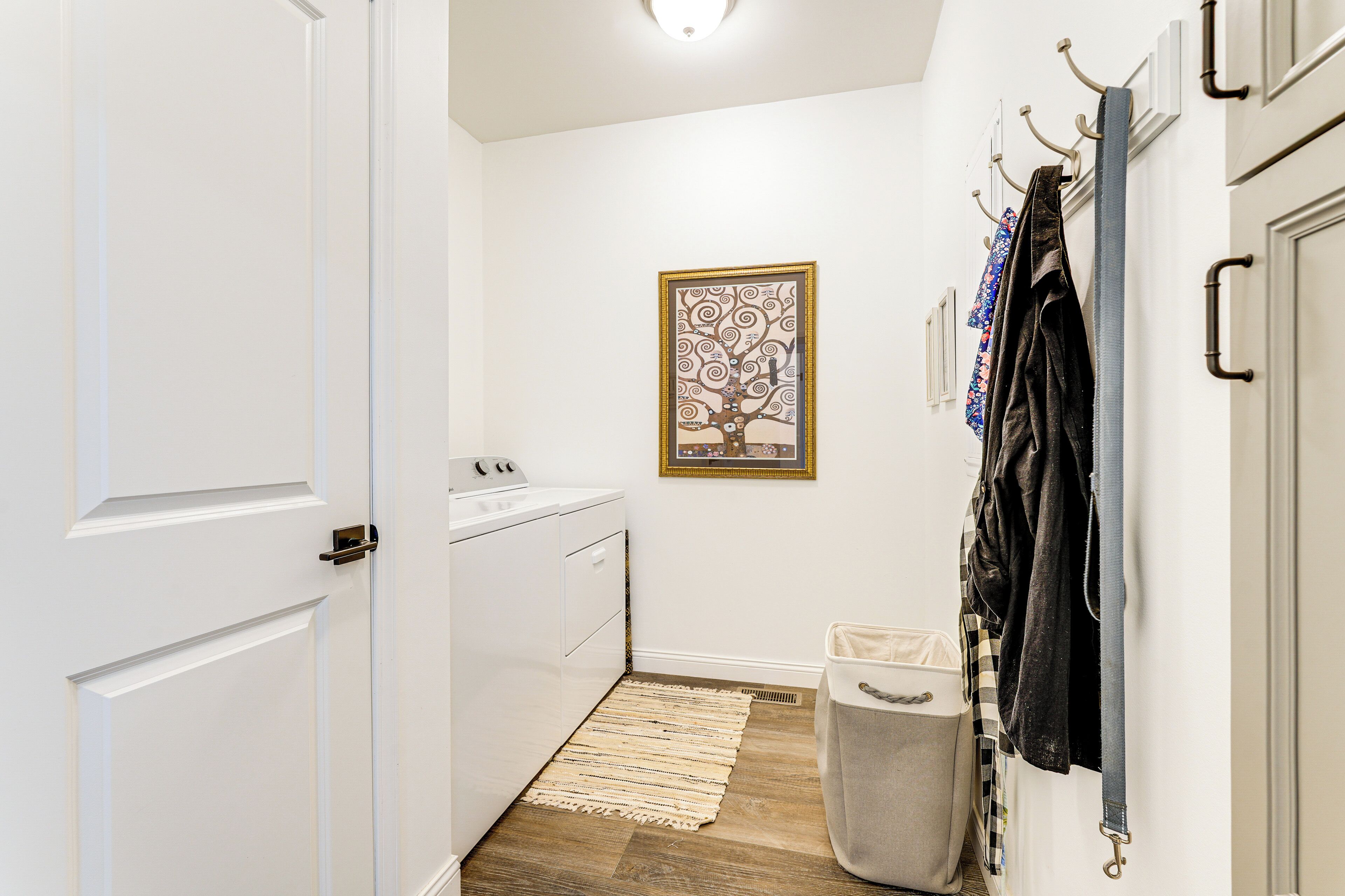 A laundry area with a washing machine, a drying rack, a trash bin, and a framed artwork on the wall.