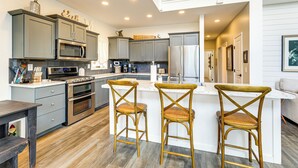 A modern kitchen with grey cabinets, stainless steel appliances, and a central island with two bar stools. - Lake Wawasee Family Getaway in Syracuse! (Syracuse)