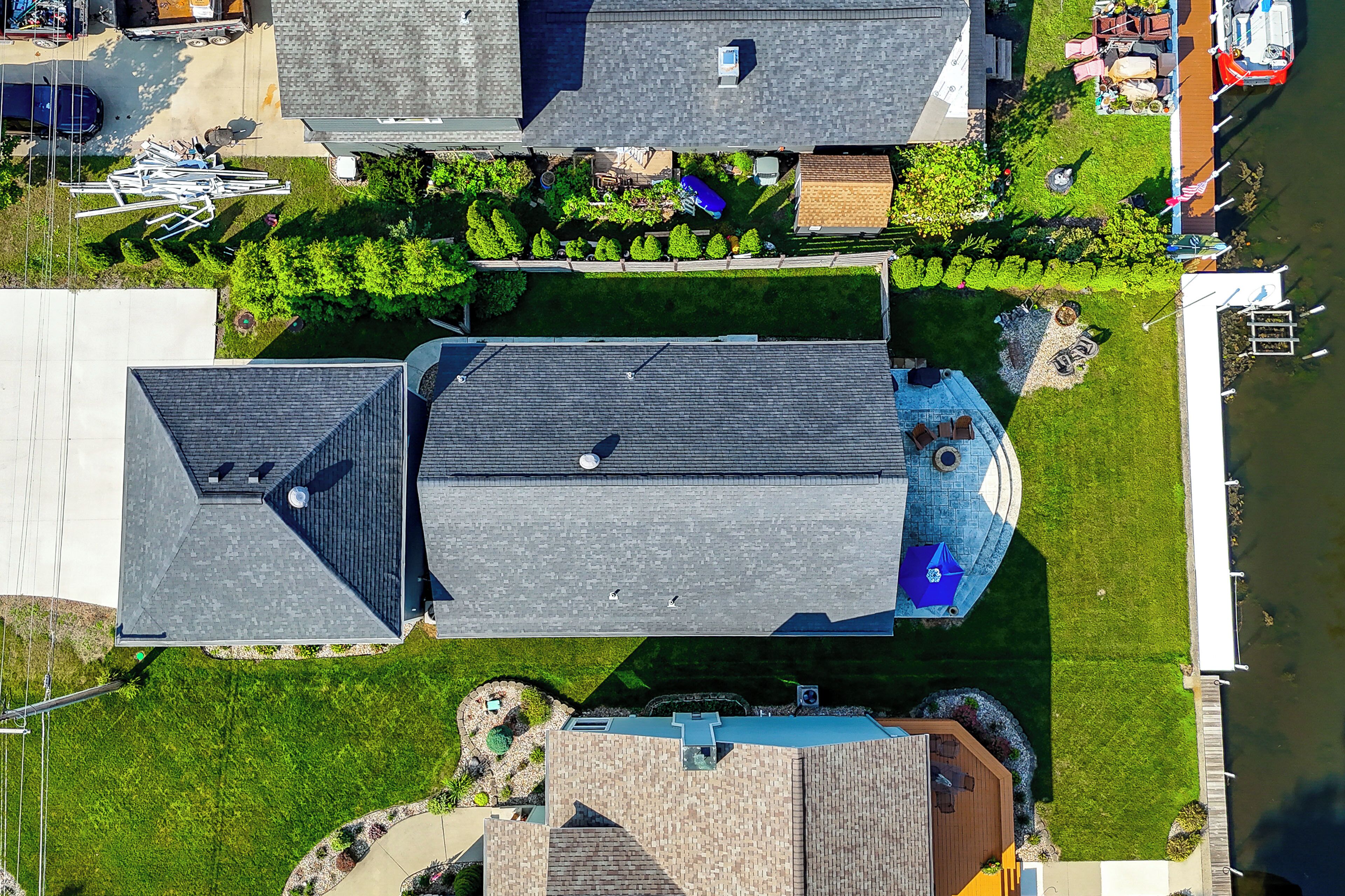 Vue aérienne d’un quartier résidentiel avec plusieurs maisons, une piscine et un quai au bord d’une étendue d’eau.