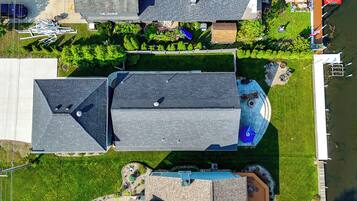 Vue aérienne d’un quartier résidentiel avec plusieurs maisons, une piscine et un quai au bord d’une étendue d’eau.