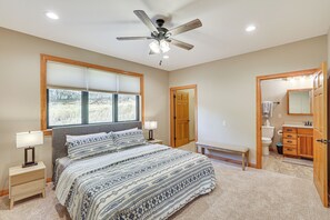 A bedroom with a bed, bedside tables, a ceiling fan, a window, and a bathroom with a toilet, sink, and mirror.