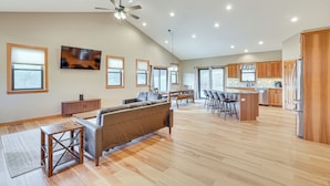 Amplia sala de estar con un sofá, una mesa de centro y una mesa de comedor con sillas. Hay una zona de cocina con armarios de madera y un refrigerador.