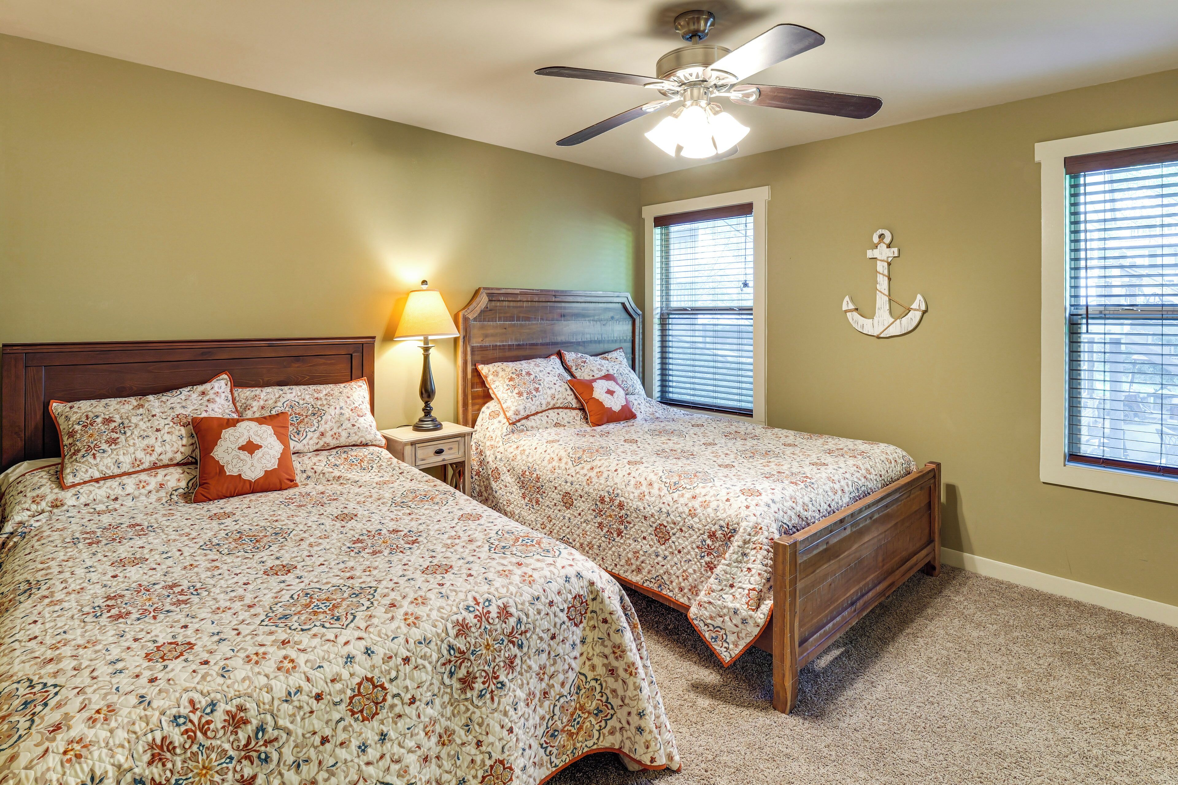 A bedroom with two beds, a ceiling fan, a nightstand with a lamp, and a window with blinds.