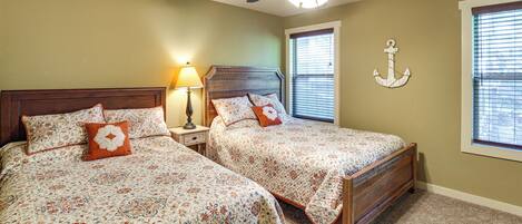 A bedroom with two beds, a ceiling fan, a nightstand with a lamp, and a window with blinds.
