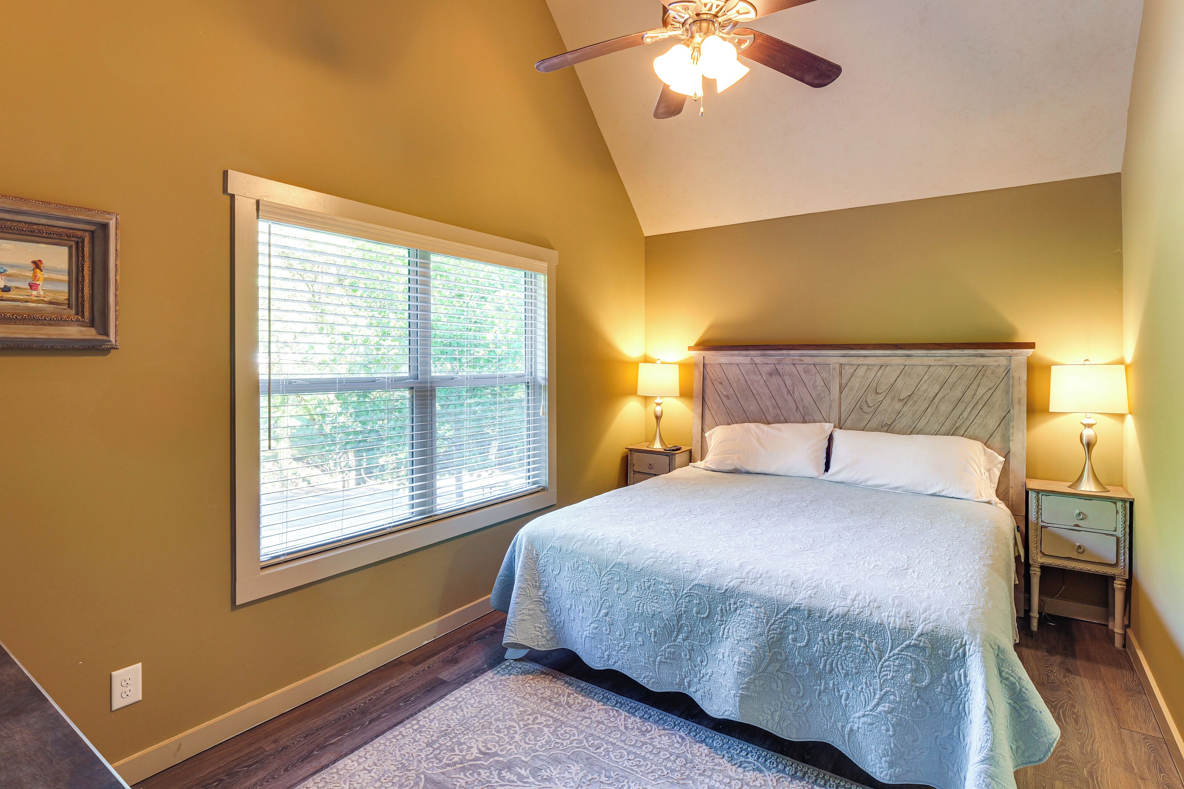 A bedroom with a large bed, two bedside tables with lamps, a ceiling fan, and a window with blinds.