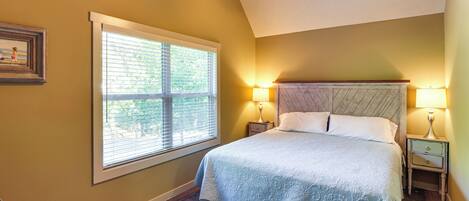 A bedroom with a large bed, two bedside tables with lamps, a ceiling fan, and a window with blinds.