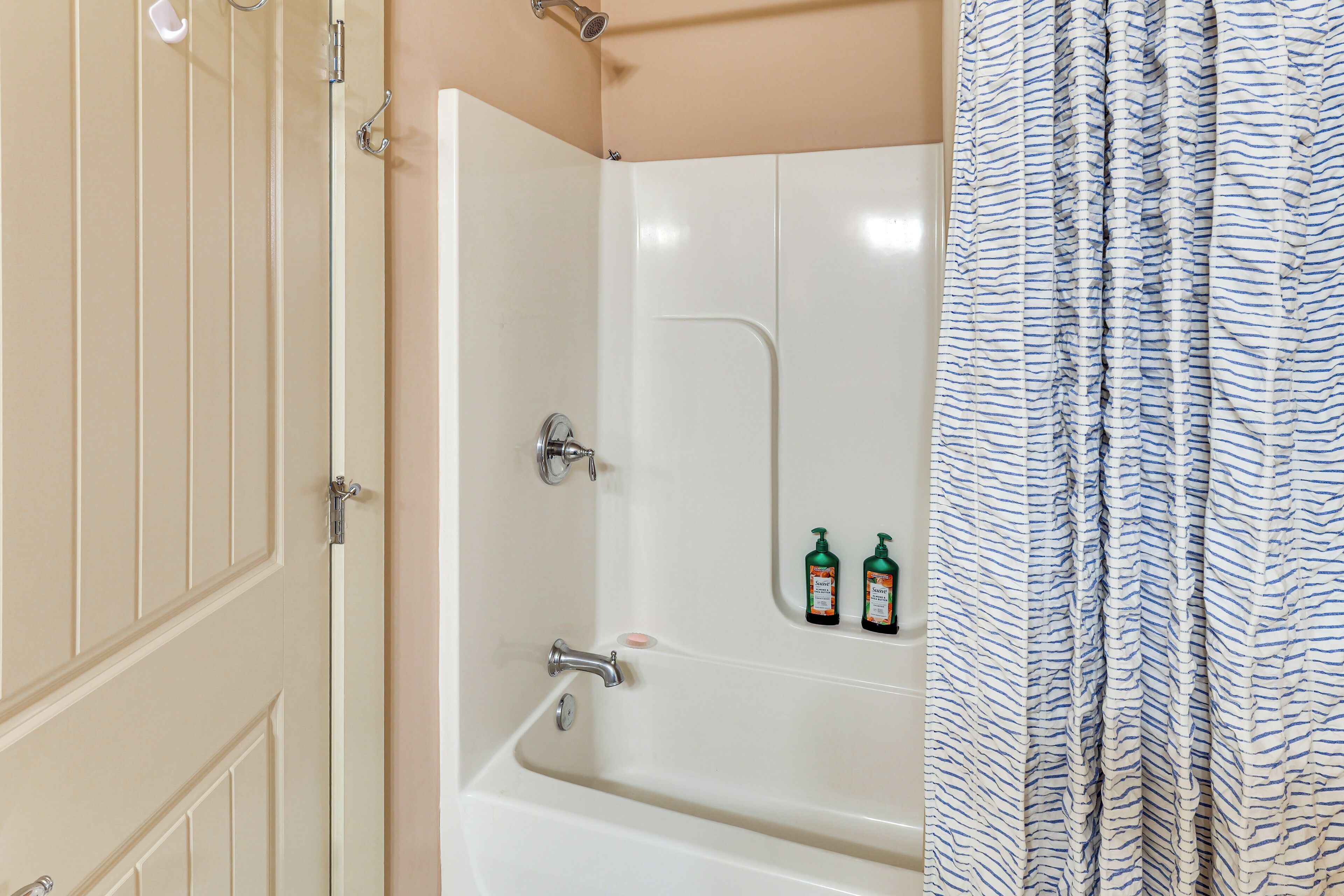 A bathroom with a bathtub, a shower, and a toilet. There are two bottles of shampoo on the wall.