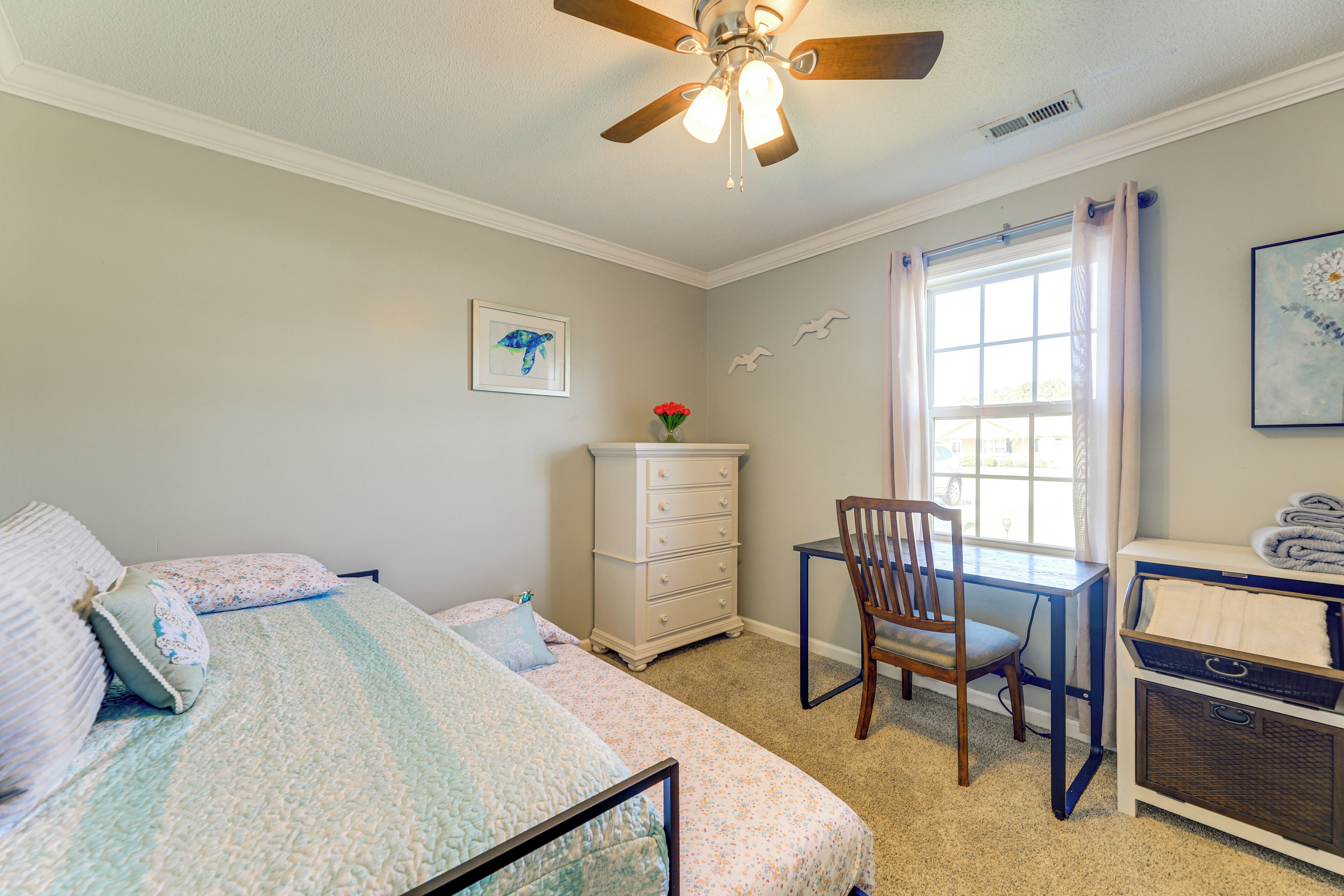 A bedroom with a bed, a desk, a chair, a dresser, and a window with curtains.