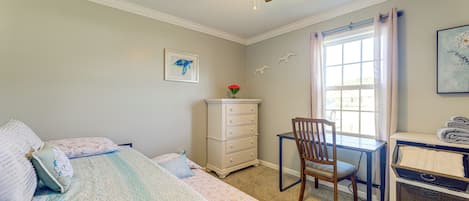 A bedroom with a bed, a desk, a chair, a dresser, and a window with curtains.
