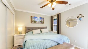 A bedroom with a bed, nightstand, bench, ceiling fan, painting, mirror, and a window with curtains. - 7 Mi to the Hammocks Beach: 3 BD Near Camp Lejeune (Hubert)