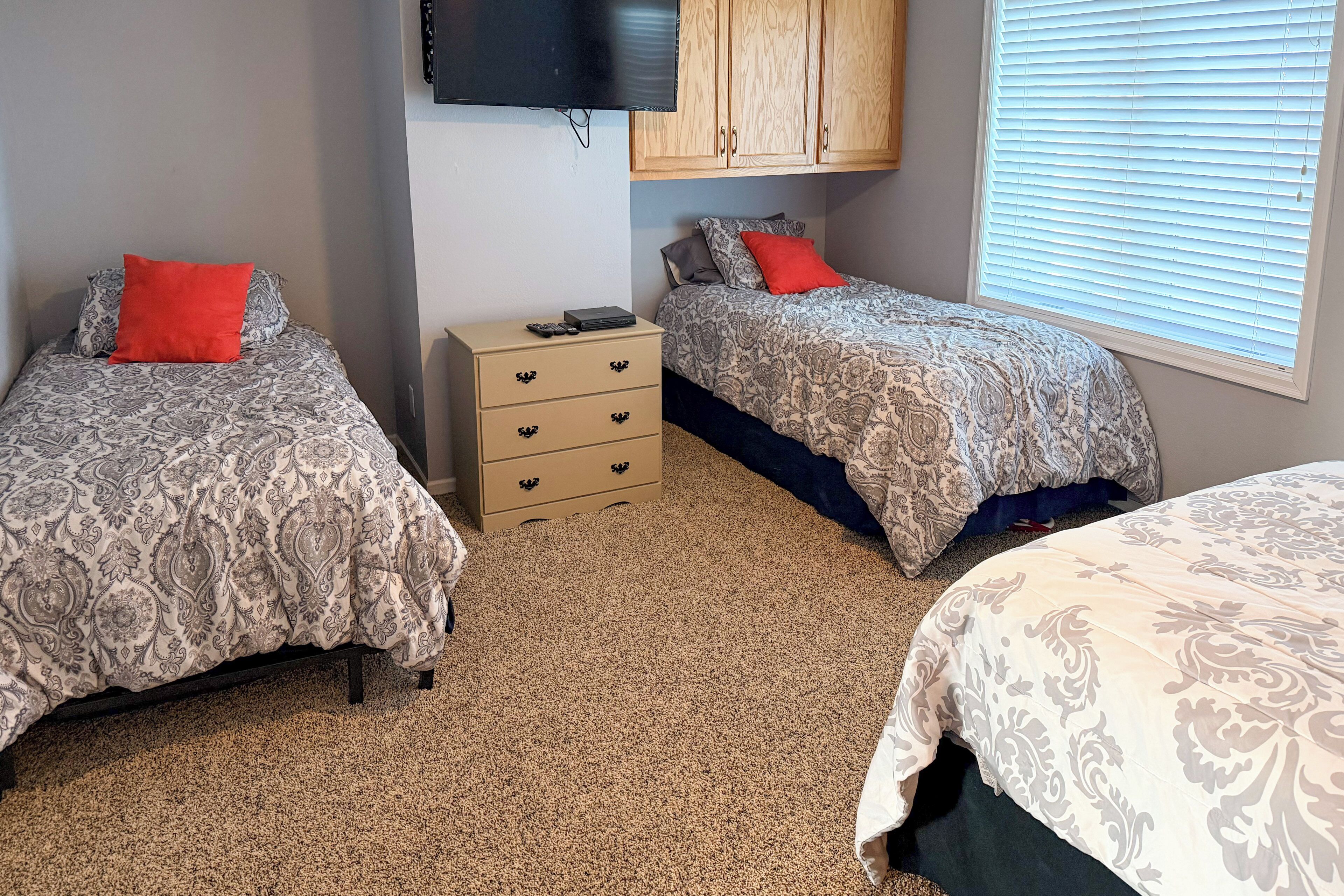 A bedroom with two beds, a dresser, a TV, and a window with blinds.
