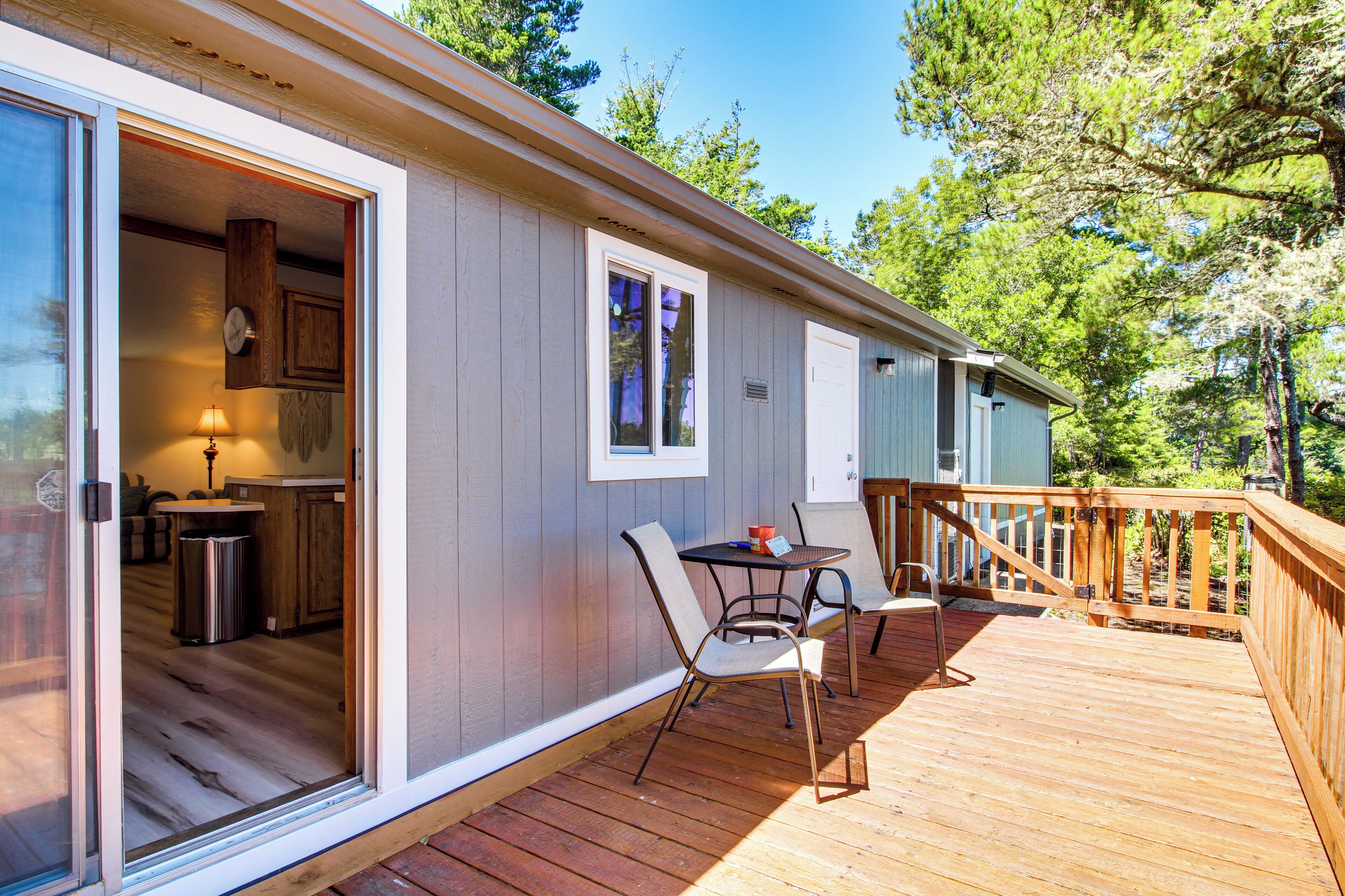 A wooden deck with a table and chairs, a sliding glass door leading to a kitchen, and a view of trees.