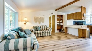 Un salon chaleureux avec un canapé et un fauteuil, un plancher en bois et un coin cuisine doté de meubles en bois.