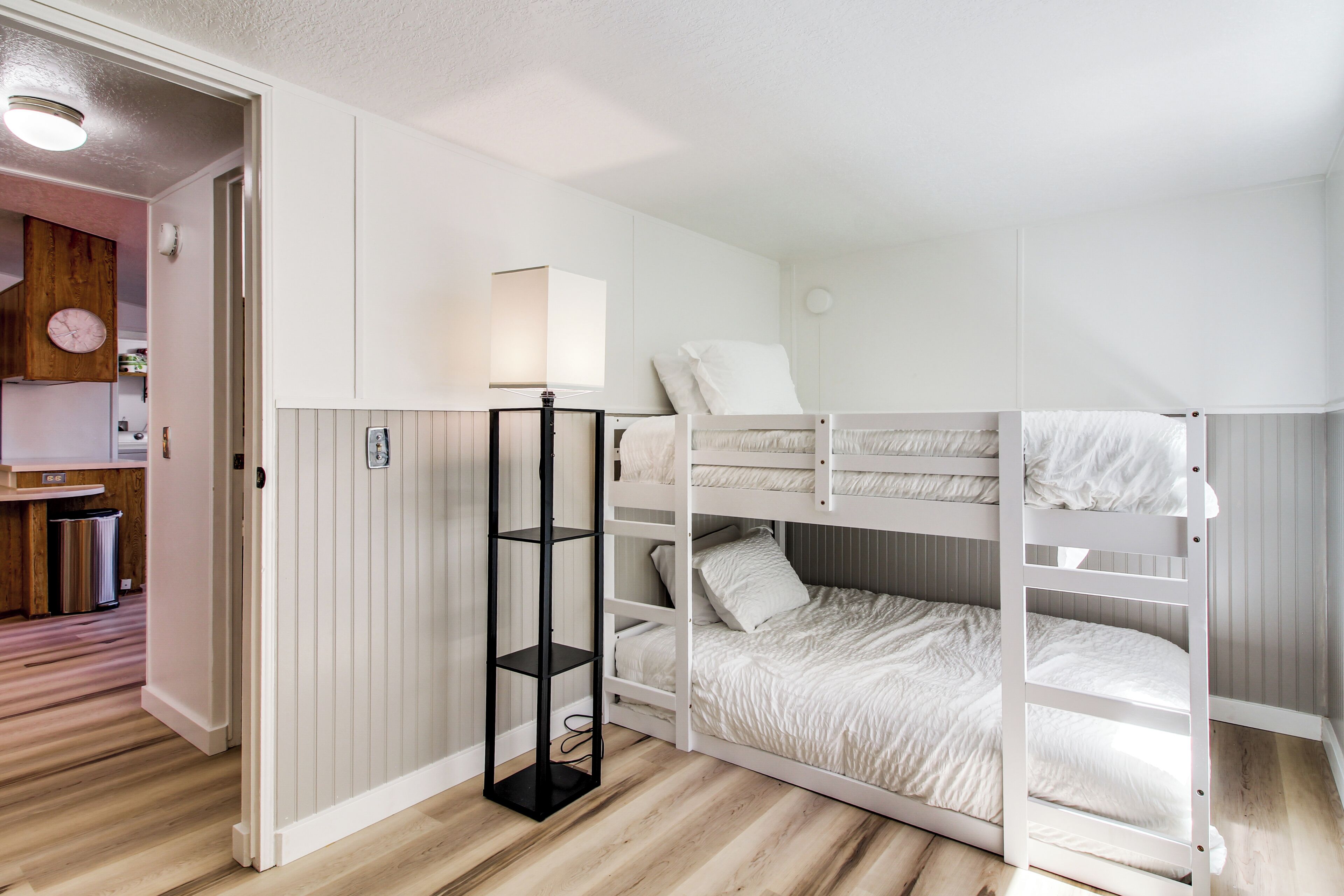 Ein Stockbett mit weißem Kopfteil, ein Nachttisch mit Lampe und ein kleines Regal.
