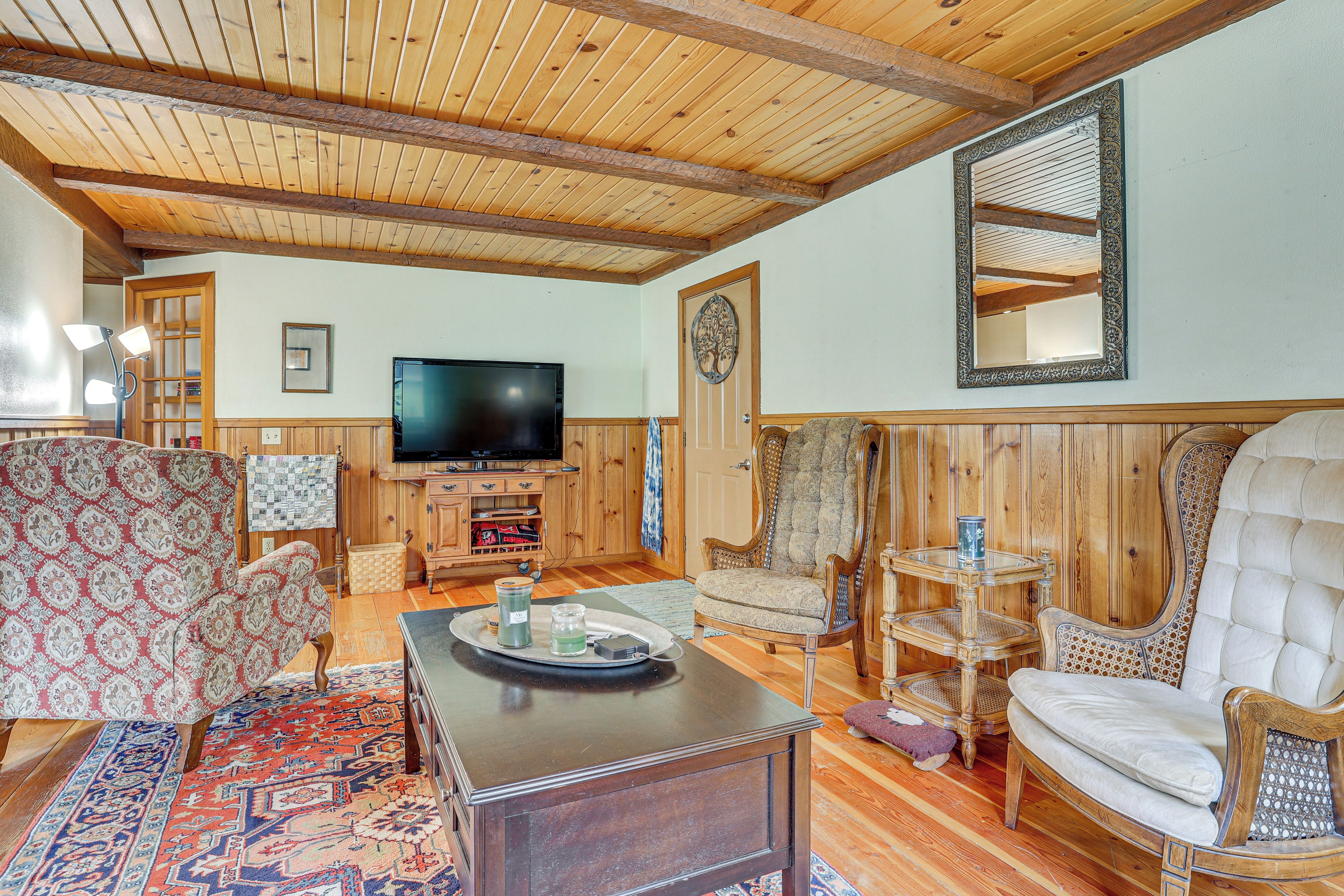 Un salón acogedor con vigas de madera, un televisor, sillones estampados y una mesa de centro.