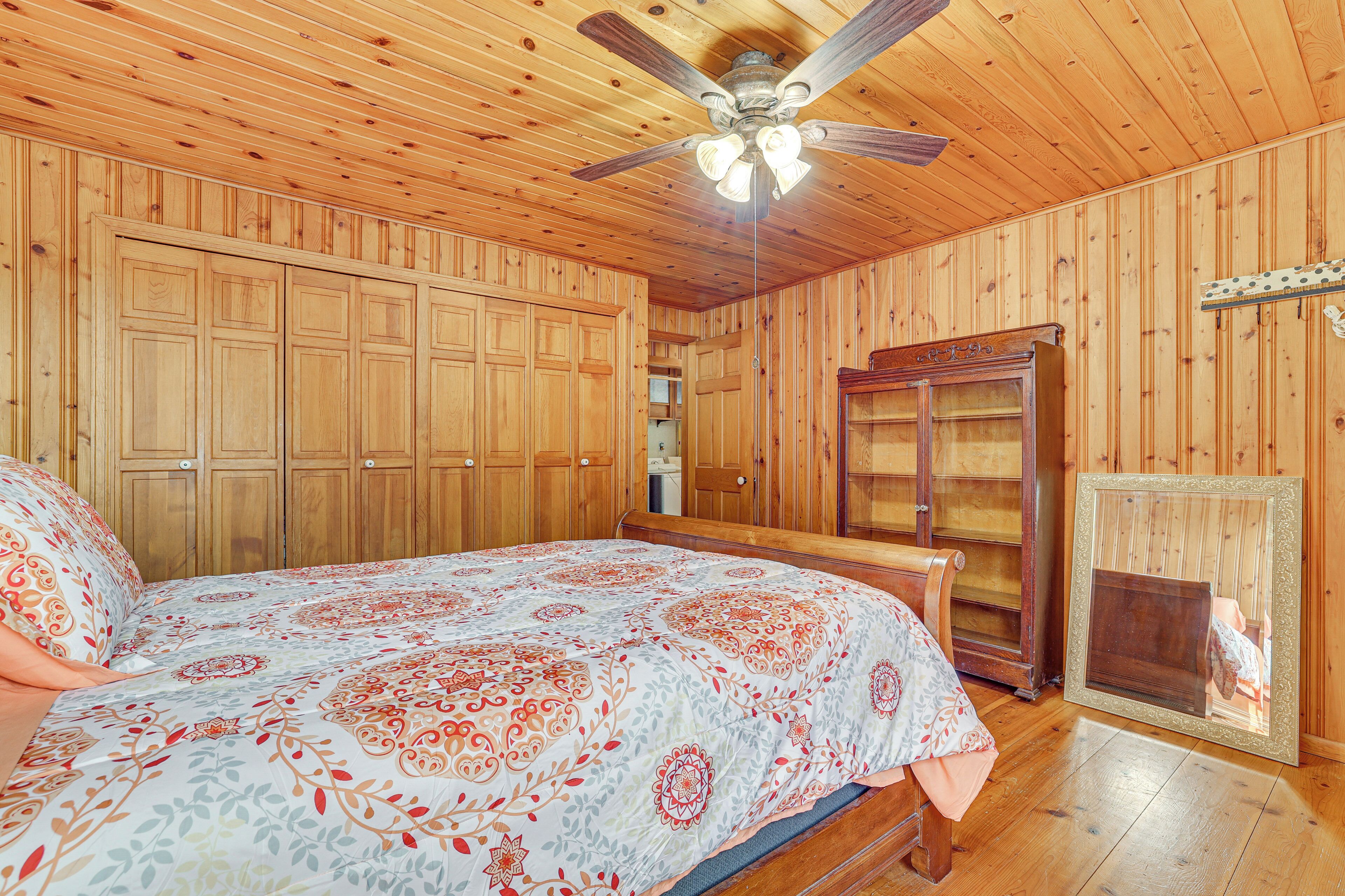 A wooden-paneled room with a bed, a ceiling fan, and a wooden cabinet.
