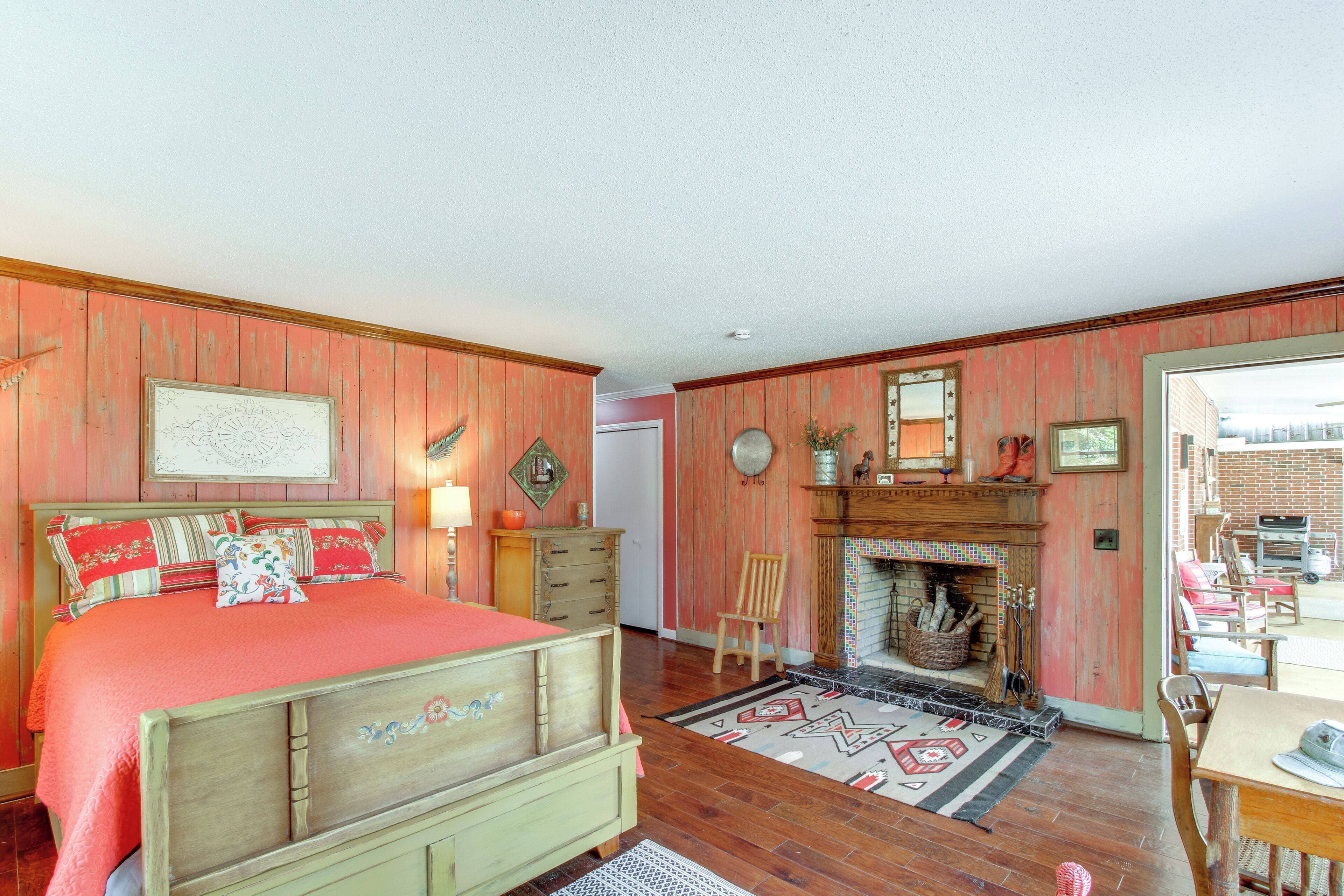 A bedroom with a bed, a dresser, a chair, a fireplace, and a view of the outside.