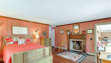 A bedroom with a bed, a dresser, a chair, a fireplace, and a view of the outside.