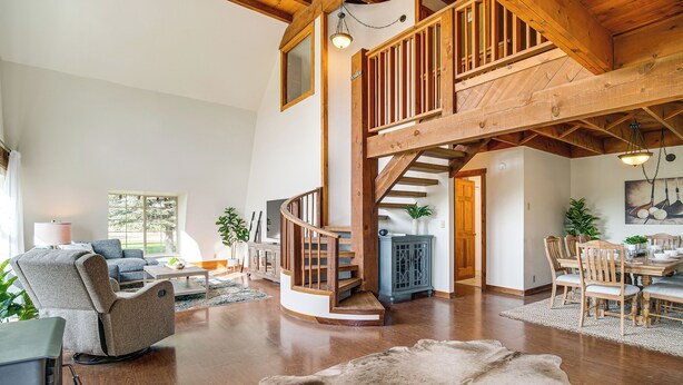 A spacious living area with a wooden staircase, a leather sofa, and a dining table with chairs. - Mtn & Golf Course View: Oregon Outback Getaway! (Lakeview)