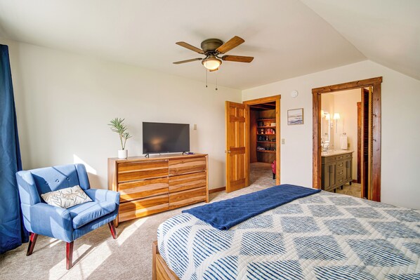 A bedroom with a bed, a blue armchair, a wooden dresser, a television, and a ceiling fan.