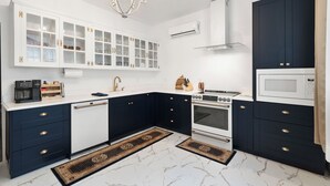 A modern kitchen with white and dark blue cabinetry, a built-in oven, microwave, and a chandelier.