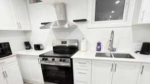 Une cuisine moderne avec des armoires blanches, une hotte de cuisinière en acier inoxydable, un four encastré et une fenêtre au-dessus de l’évier.