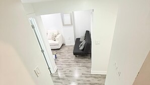 Un escalier mène à un espace de vie doté d’un parquet en bois foncé, de murs blancs et d’un canapé noir agrémenté de coussins à motifs.