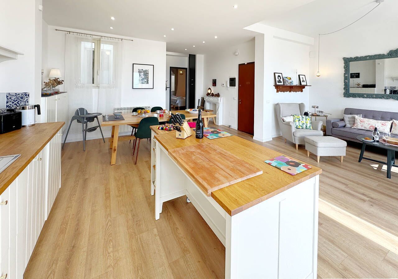 Eine moderne Küche mit Holzarbeitsplatte, ein Essbereich mit Stühlen und ein Wohnzimmer mit Sofa und Couchtisch.
