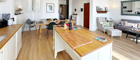 Une cuisine moderne avec un plan de travail en bois, un coin repas avec des chaises et un salon avec un canapé et une table basse.