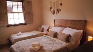 A room with two beds, each with a headboard and pillows, a window with lace curtains, and a wall hanging. - Recanto das Libelulas pousada (Tiradentes)