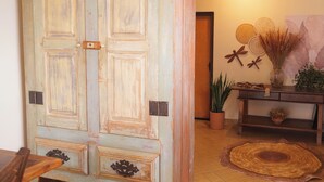 A room with a large wooden door, a console table with decorative items, and a woven rug. - Recanto das Libelulas pousada (Tiradentes)