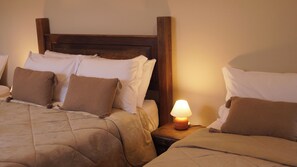 A hotel room with two beds, each with a wooden headboard, white and brown pillows, and a bedside table with a lamp.