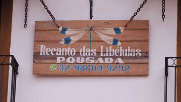 A wooden sign with a dragonfly design and text reading "Recanto das Libélulas Pousada" along with a phone number.