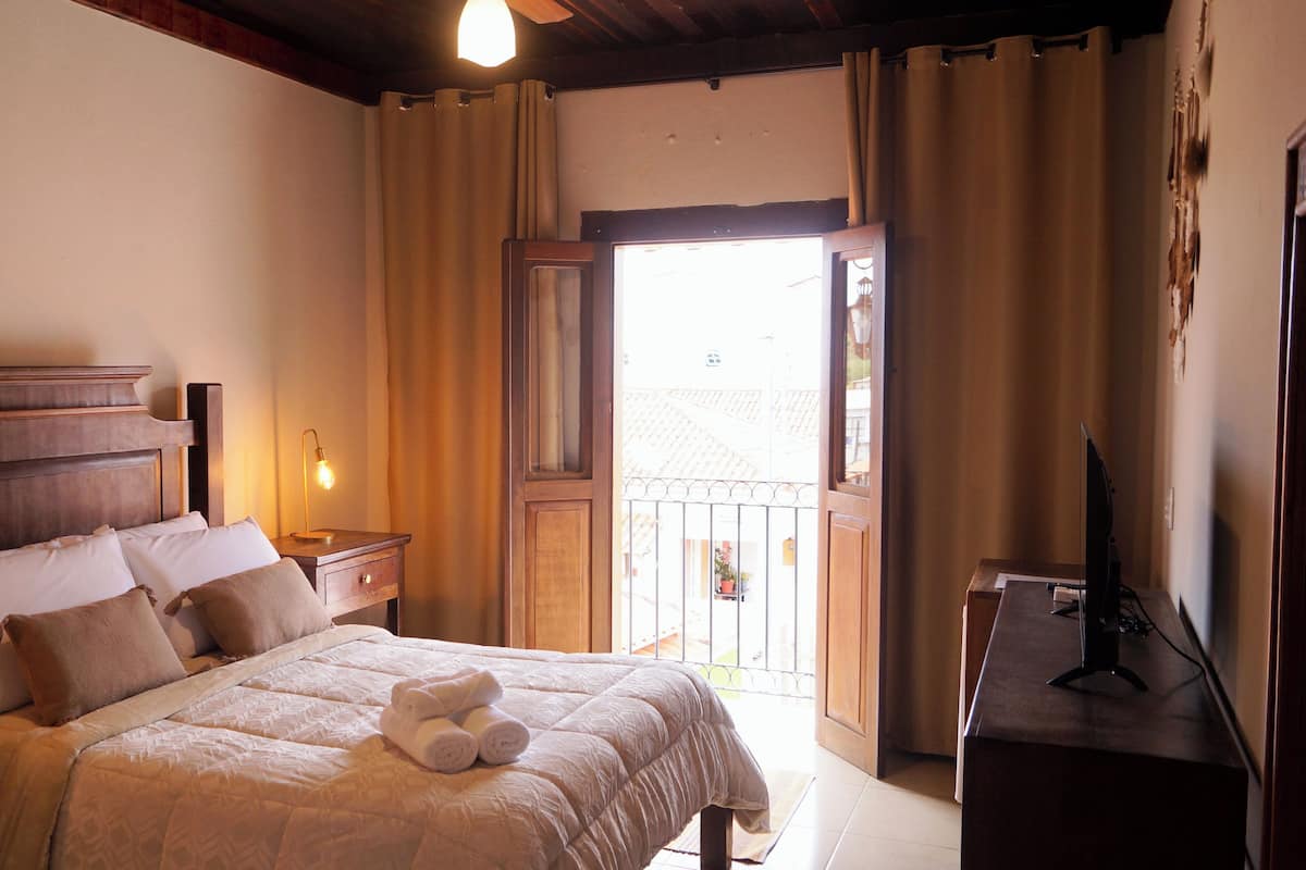 A bedroom with a bed, bedside table, lamp, and a desk with a computer.