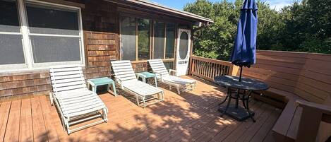 A wooden deck with lounge chairs and a table, overlooking a garden.