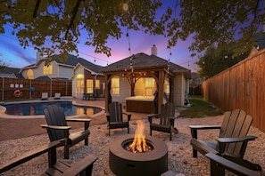 A backyard with a hot tub, outdoor seating, and a fire pit.