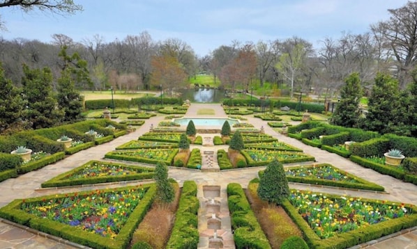 A formal garden with symmetrical pathways, a central water feature, and neatly trimmed hedges.