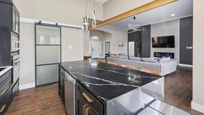 A modern kitchen with a large island, built-in appliances, and a seating area with a grey sofa and orange chairs. - 5-BD/2-BA Vacation Retreat w/ Pool, Hot Tub & BBQ (Haltom City)