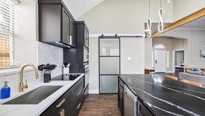 A modern kitchen with black cabinets, a marble countertop, and a central island. - 5-BD/2-BA Vacation Retreat w/ Pool, Hot Tub & BBQ (Haltom City)