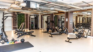 A modern gym with various exercise equipment, including treadmills and weight machines, and a mirrored wall reflecting the equipment.