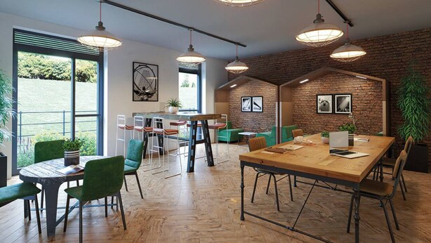 A modern office space with a large wooden table, green chairs, and hanging pendant lights.