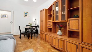 Une pièce dotée d’un parquet en bois disposé en chevrons, d’un canapé gris, d’une table à manger avec des chaises, et d’un meuble en bois avec des portes en verre.