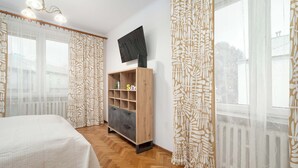 Une chambre à coucher avec un lit, une armoire en bois, une télévision et des rideaux en voile.