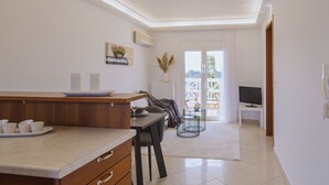 A modern kitchen with a dining area, a TV, and a balcony with a view. - Perdika Residences (Aegina)