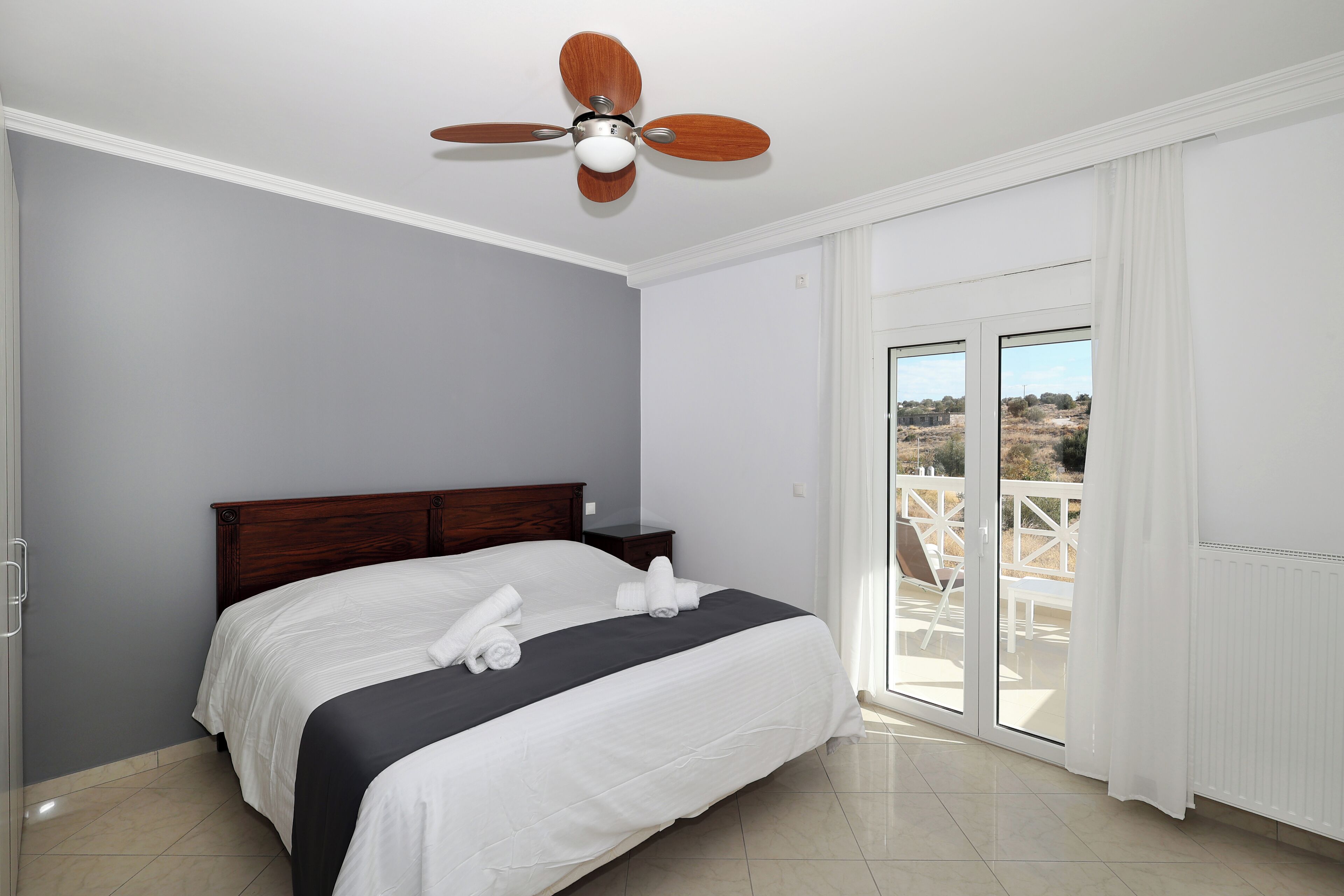 A bedroom with a bed, a ceiling fan, a nightstand, and a view of the outdoors through a sliding glass door.