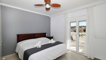 A bedroom with a bed, a ceiling fan, a nightstand, and a view of the outdoors through a sliding glass door.