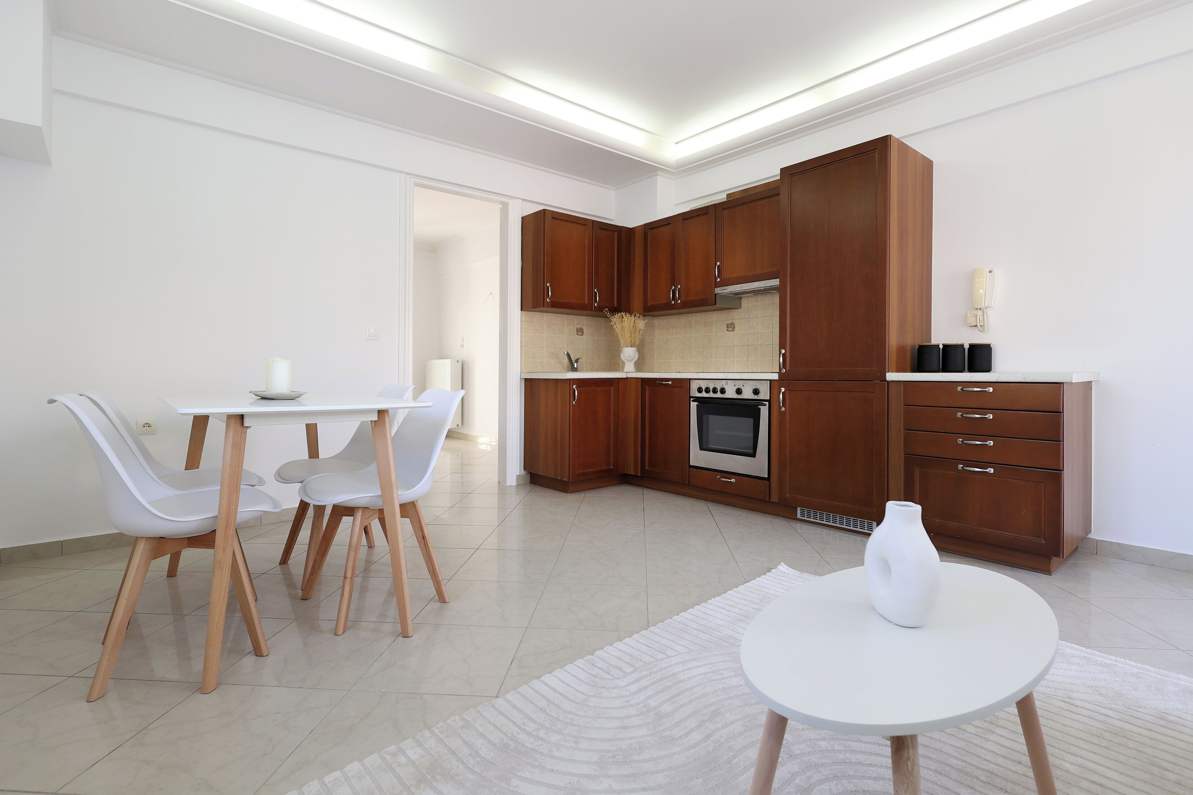 Une cuisine moderne avec des meubles en bois, un plan de travail blanc et un coin repas comprenant des chaises blanches et une petite table.