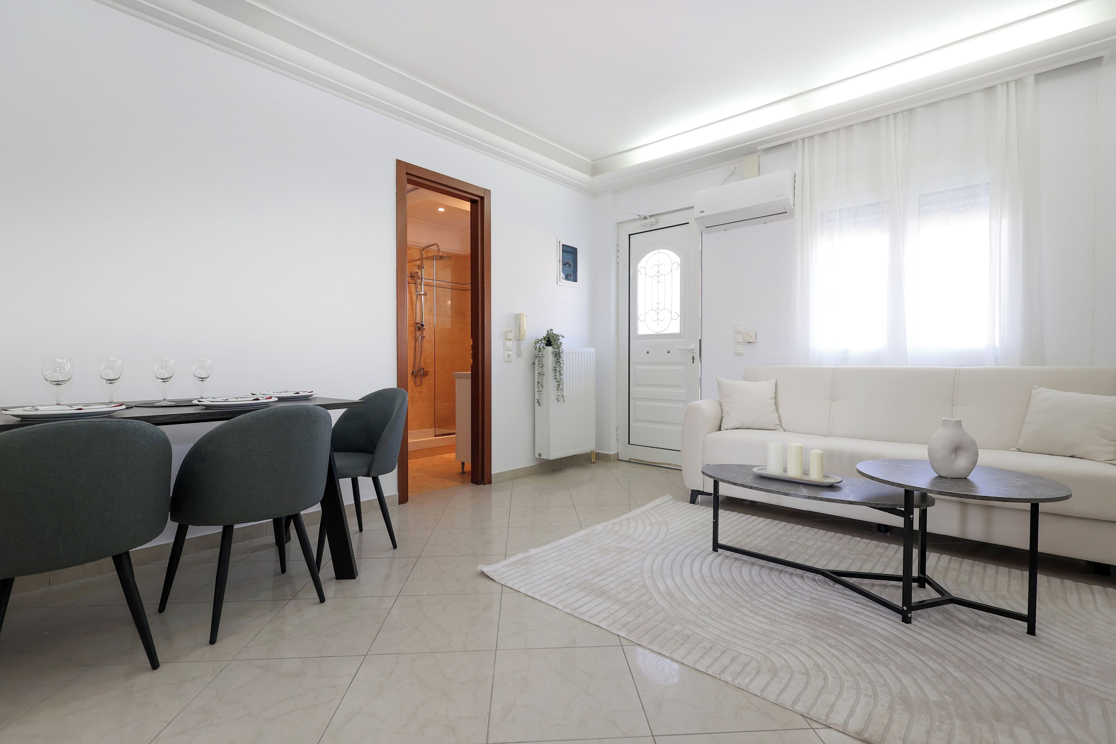 Uma sala de estar moderna com área de jantar, paredes brancas e uma grande janela.