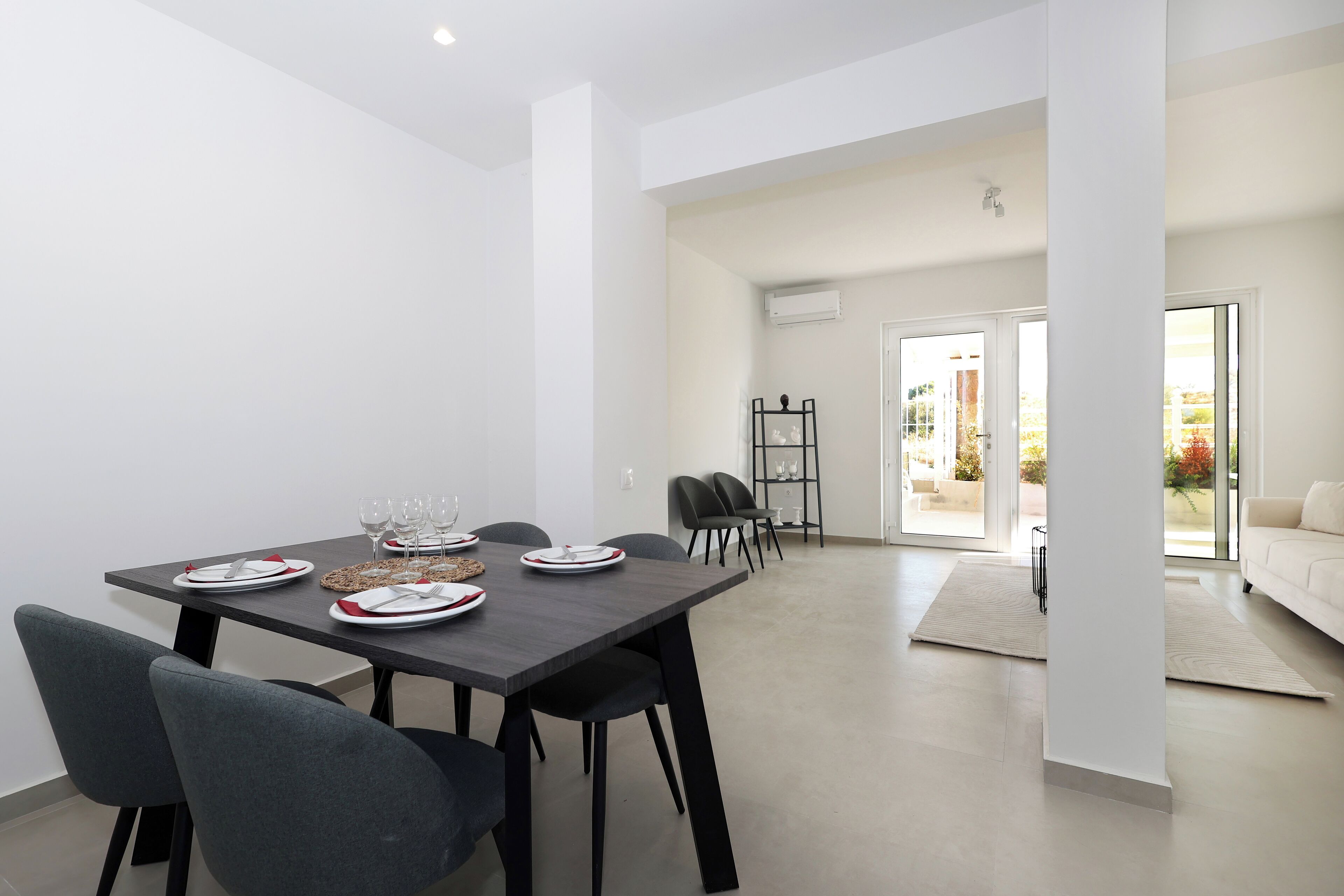 A modern dining area with a dark wooden table set for four, surrounded by grey chairs.
