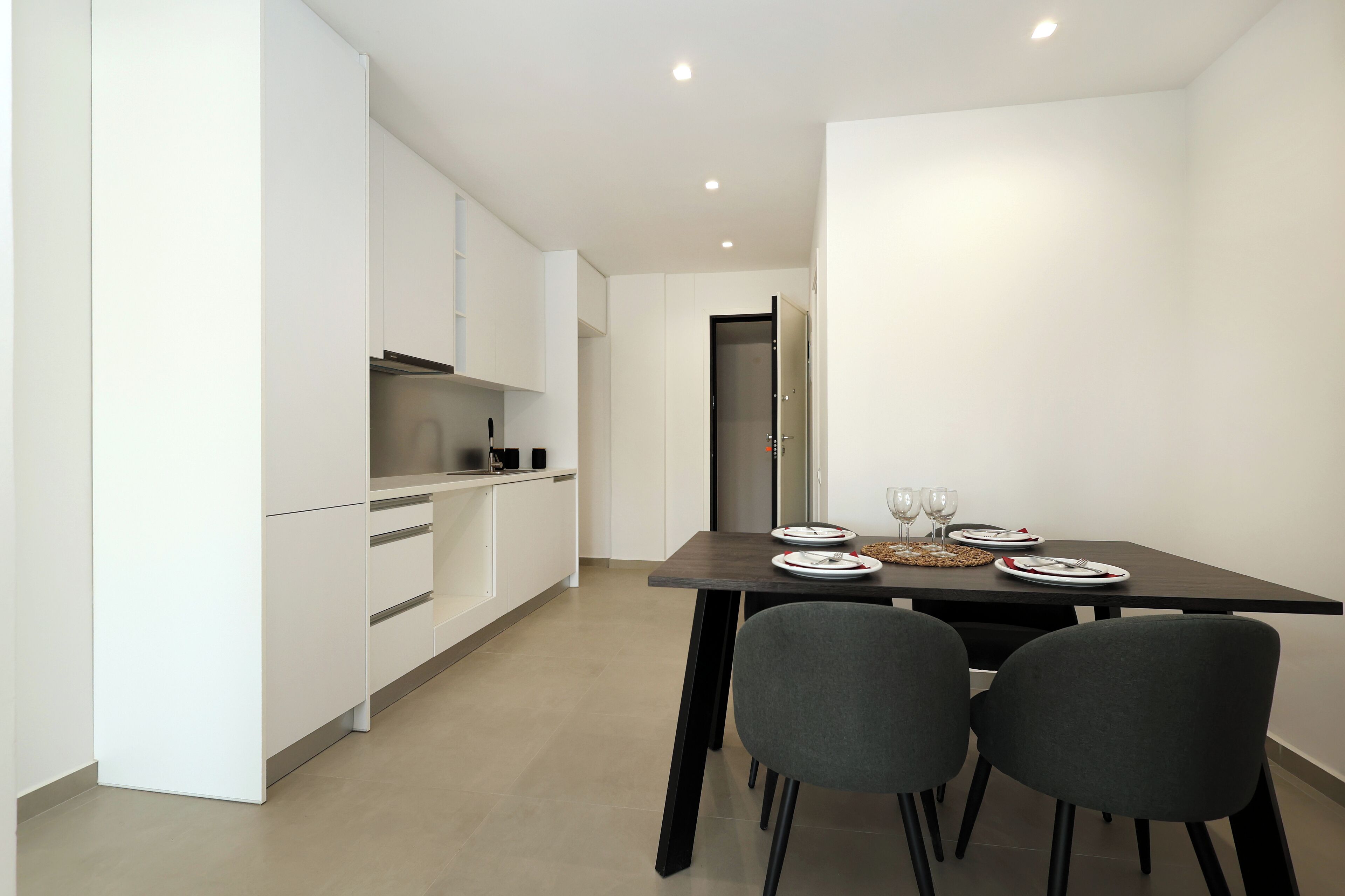 Una cocina moderna con armarios blancos, un comedor oscuro y dos sillas grises.